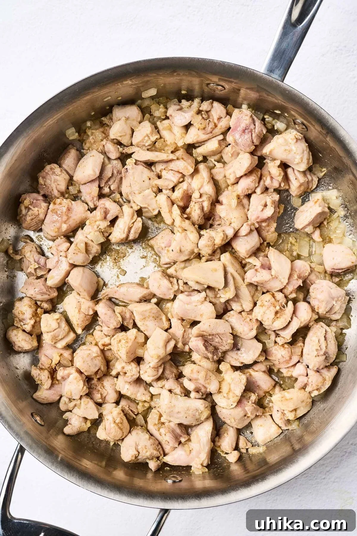 Velvety African Peanut Chicken Pot 4 Bite-sized pieces of boneless chicken thighs are being skillfully sautéed in a large skillet alongside finely chopped onion, minced garlic, and fresh ginger. This initial step creates a fragrant and savory aromatic base for the rich stew.