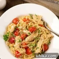 A shallow bowl of spaghetti tossed with tender strips of boneless chicken, thin spaghetti, sweet grape tomatoes, and a fresh lemon and garlic pan sauce, parsley garnish on the top.