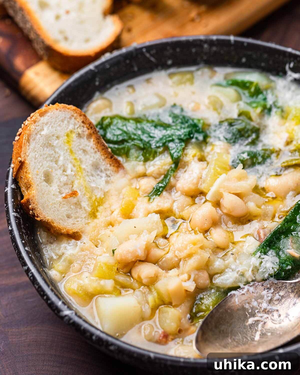 Soulful Escarole and Bean Comfort 8 A inviting black bowl brimming with creamy escarole and white bean soup, with a piece of artisanal crusty bread perfectly dipped into the rich broth, ready to be enjoyed.