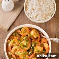 An overhead view of a bowl of Louisiana style shrimp stew in gravy with a bowl of steamed white rice and salt and pepper shakers to the rear and side.