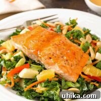 A composed salad of kale, carrots, apple, orange, red bell pepper, and cashews topped with a serving of roasted salmon with Thai-chili and orange dressing.