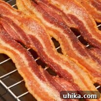 Crispy Bacon Perfection Baked in Your Oven 3 Crispy strips of baked bacon lined up on a rack inside a sheet pan.