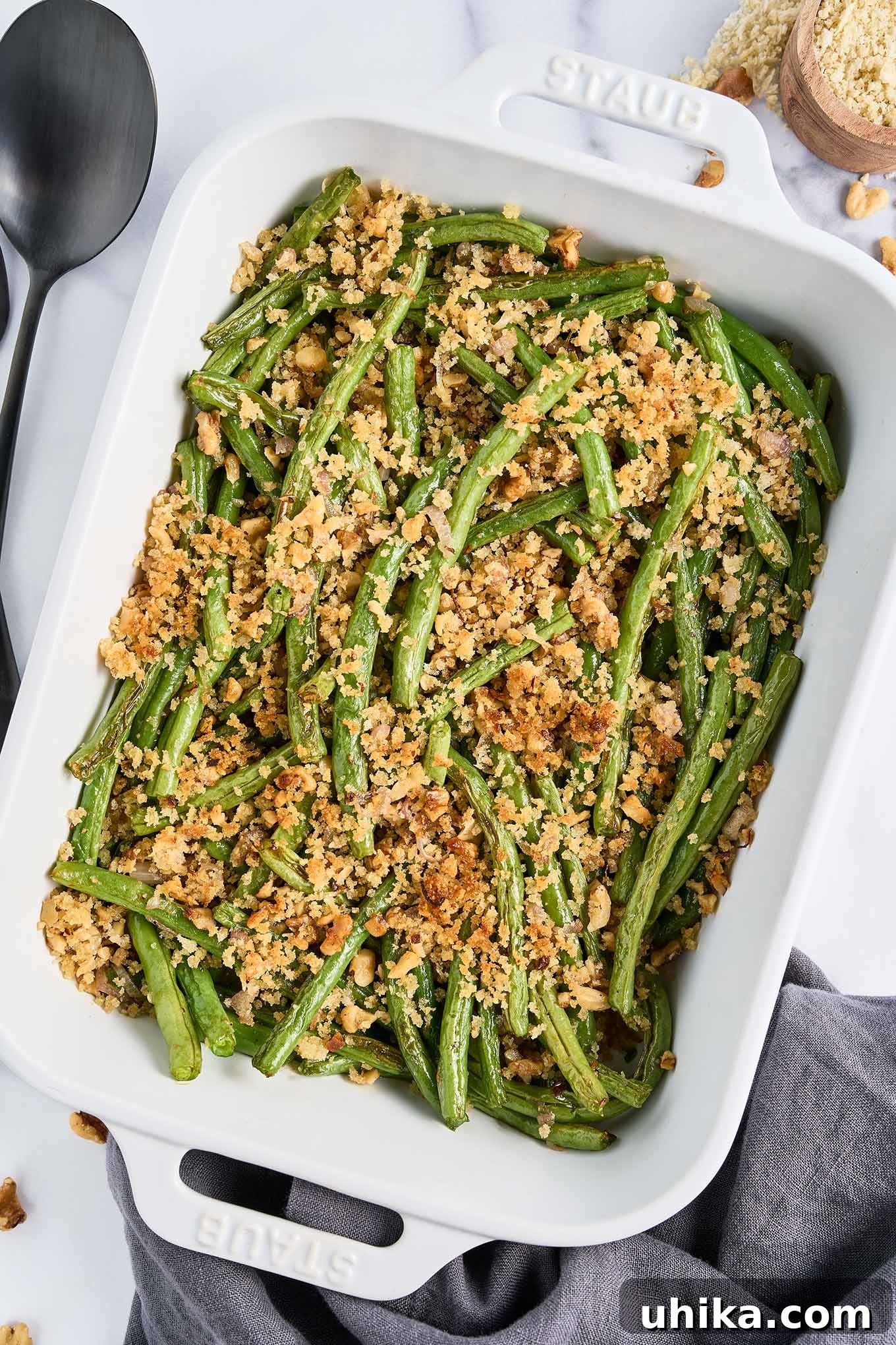 Crunchy Roasted Green Beans with Toasted Walnuts 2 A white baking dish with fresh green beans, roasted and topped with crispy walnuts and panko crumbs, ready to serve.