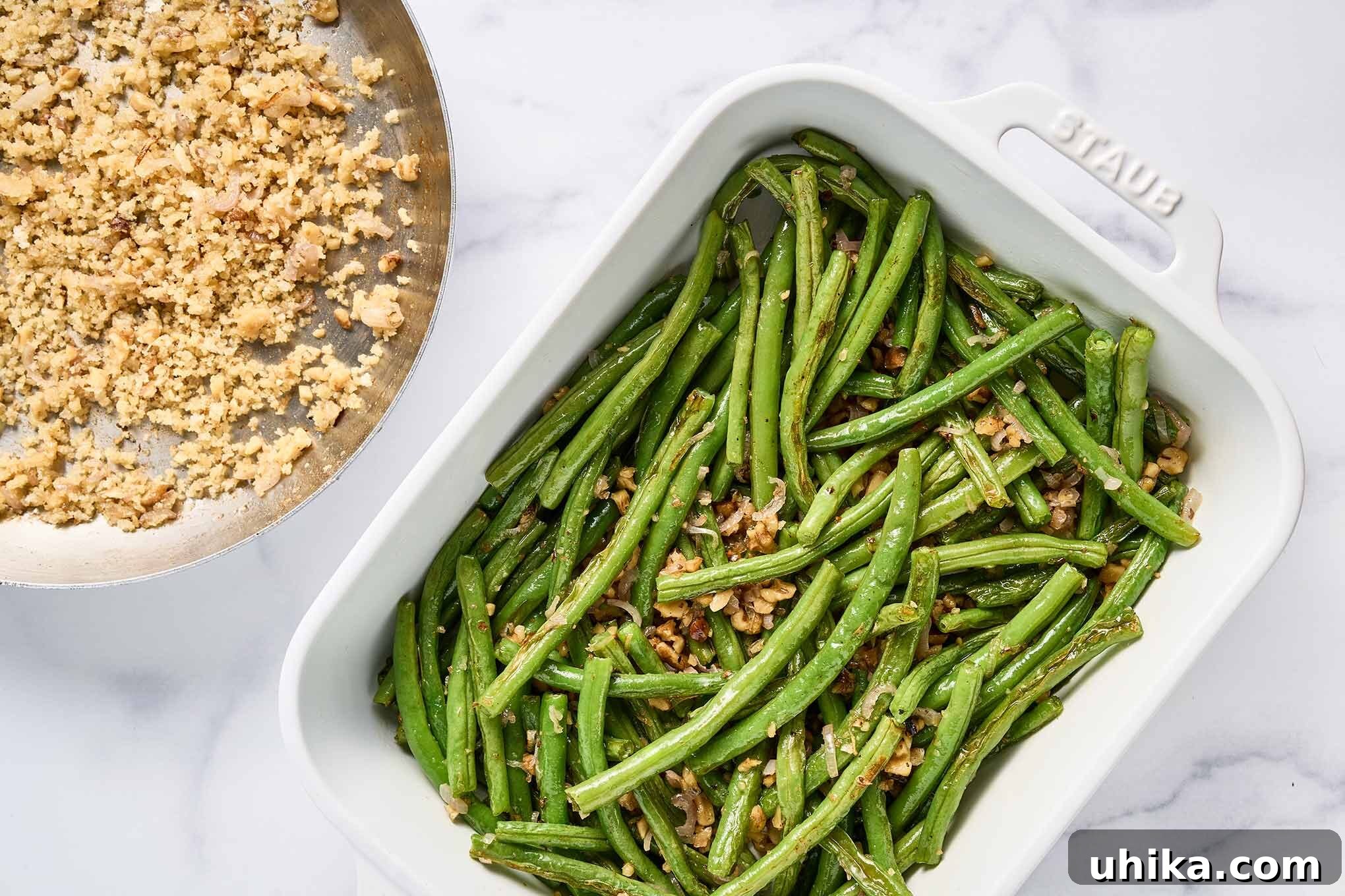 Crunchy Roasted Green Beans with Toasted Walnuts 5 Roasted green beans mixed with sautéed shallots and walnuts in a white baking dish, with a separate skillet holding the panko and walnut topping.