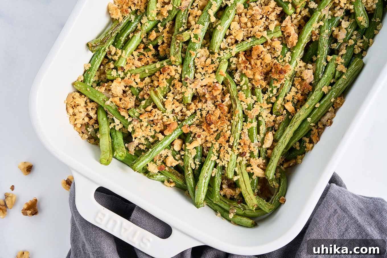 Crunchy Roasted Green Beans with Toasted Walnuts 6 A vibrant white casserole dish filled with roasted green beans, elegantly finished with a golden, crisp topping of buttery walnuts and panko crumbs, ready for serving.