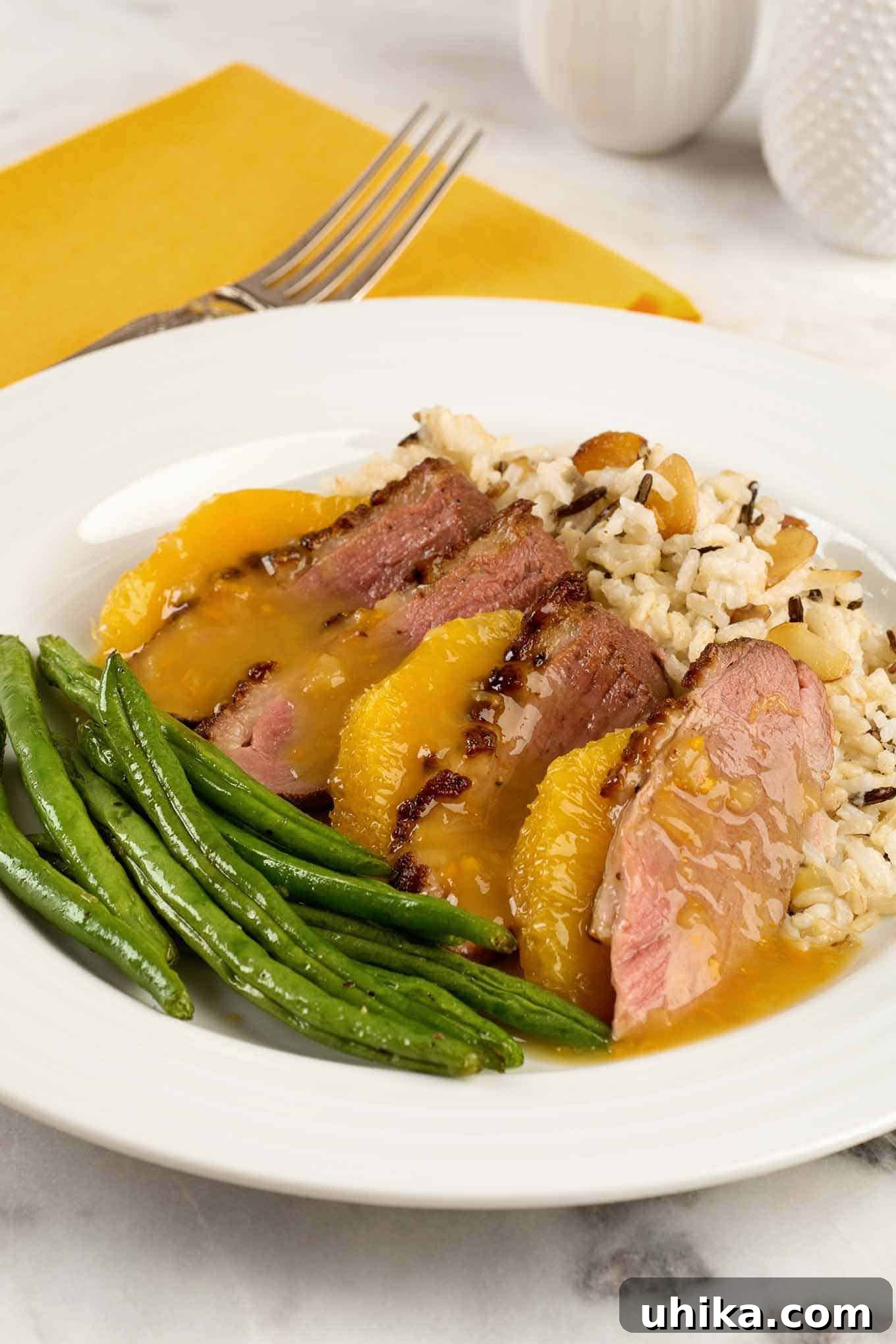 Orange Glazed Duck Breast 2 A plate with a serving of duck breast a l\'orange; sliced duck breast, medium rare, orange supremes, rice pilaf, and green beans.