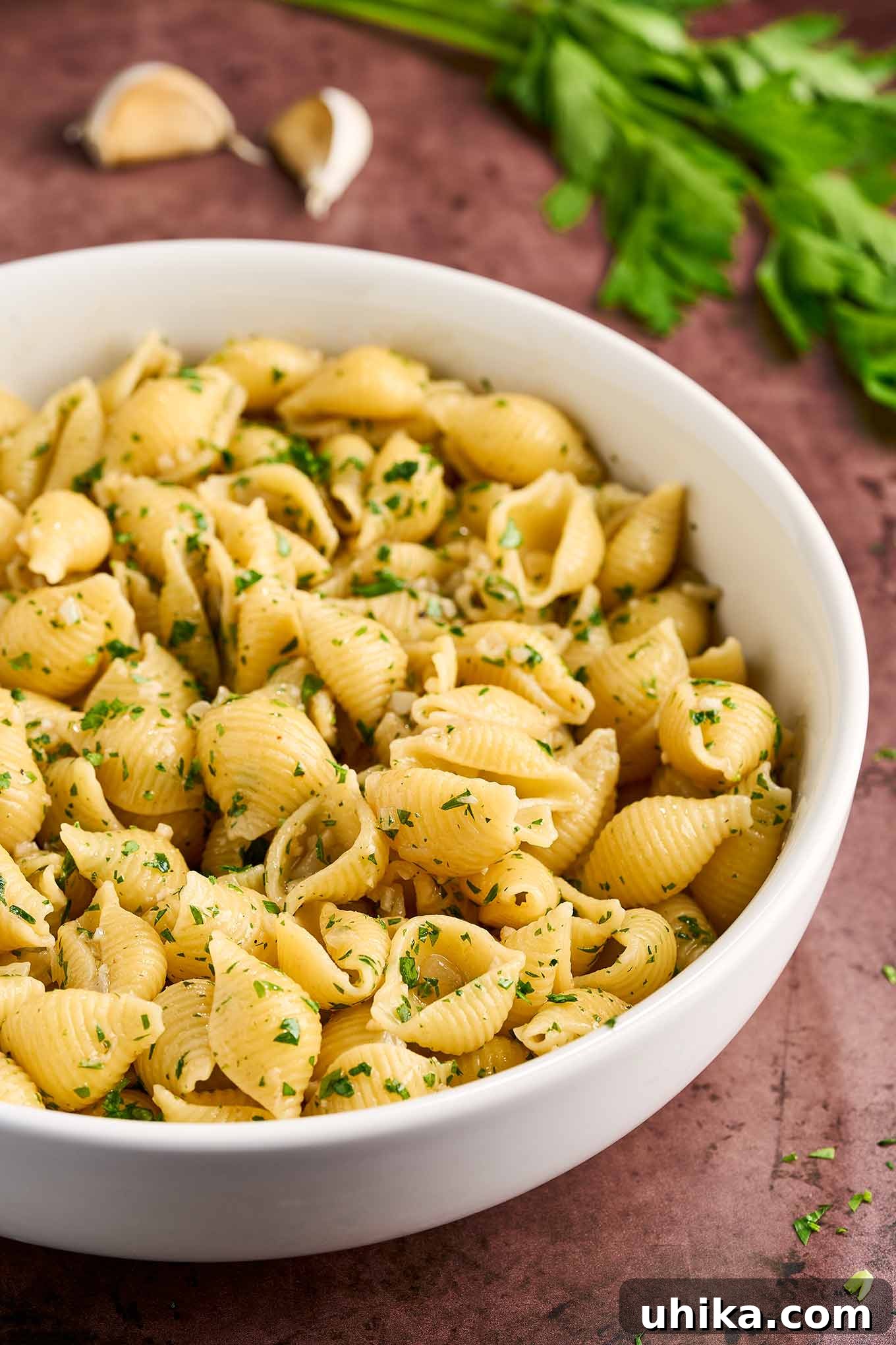 Buttery Garlic Shell Pasta 4 Steaming hot, medium pasta shells coated in a rich garlic butter sauce and sprinkled with vibrant green parsley, served in a white bowl.