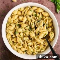 White bowl filled with cooked pasta shells tossed in garlic butter with balsamic vinegar, garnished with chopped parsley.