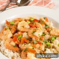 A shallow bowl of steamed rice topped with shrimp in coconut milk with red pepper, tomato, scallions, cilantro and lime, fork and spoon on a napkin in the background.