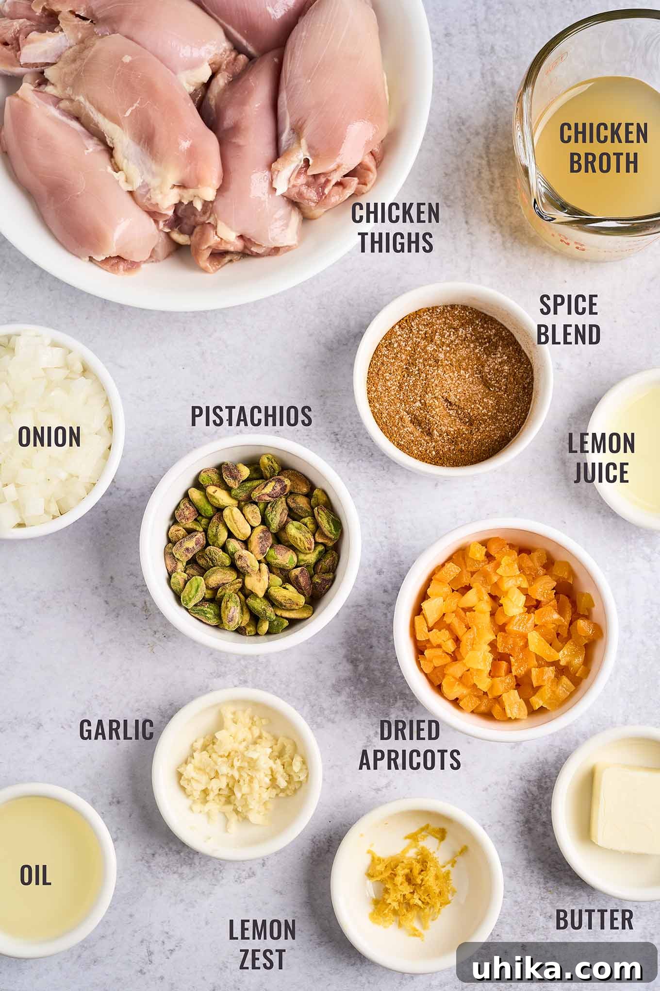 Jeweled Apricot Pistachio Chicken 3 A labeled, overhead view of the ingredients for Persian apricot chicken; boneless, skinless chicken thighs, chicken broth, spice blend, lemon juice and zest, dried apricots, butter, garlic, oil, and chopped onion.
