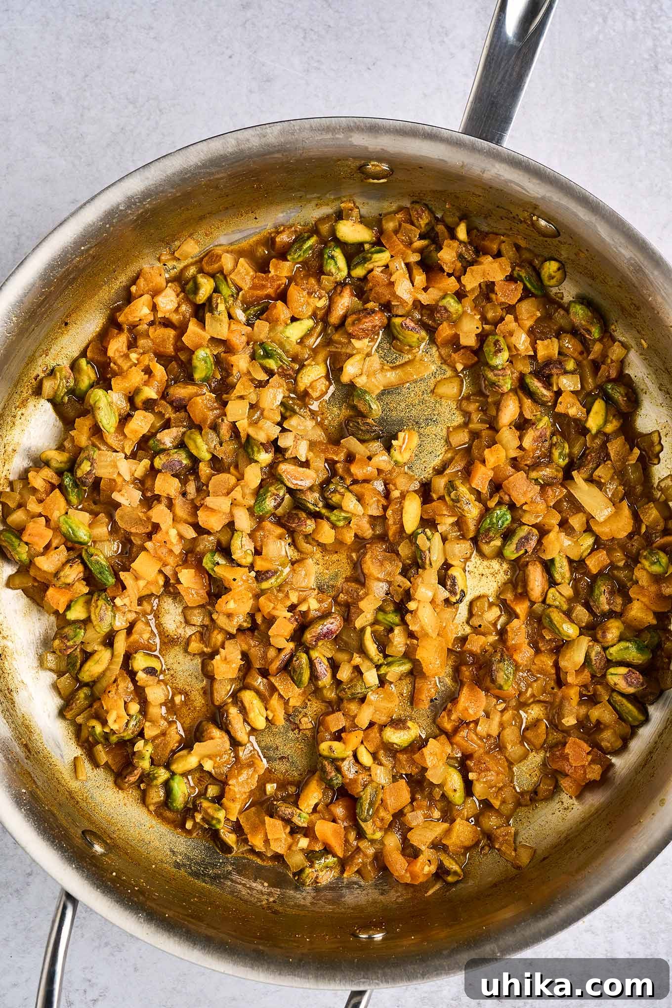 Jeweled Apricot Pistachio Chicken 4 A frying pan with sautéed onion and garlic, diced dried apricots, and pistachio nuts seasoned with a blend of salt, sugar, turmeric, coriander, cumin, cinnamon, cayenne, and black pepper.