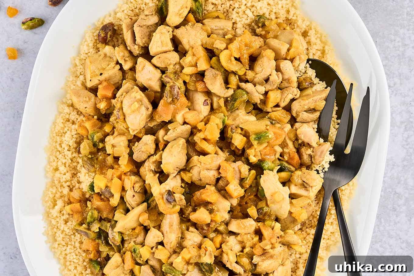 Jeweled Apricot Pistachio Chicken 6 A close view of a platter of couscous topped with Persian-style apricot chicken, showing chopped pistachios, diced dried apricots, and lemon zest.