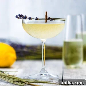 Glass of Lavender French 75 with champagne flutes, lemons and lavender in the background.