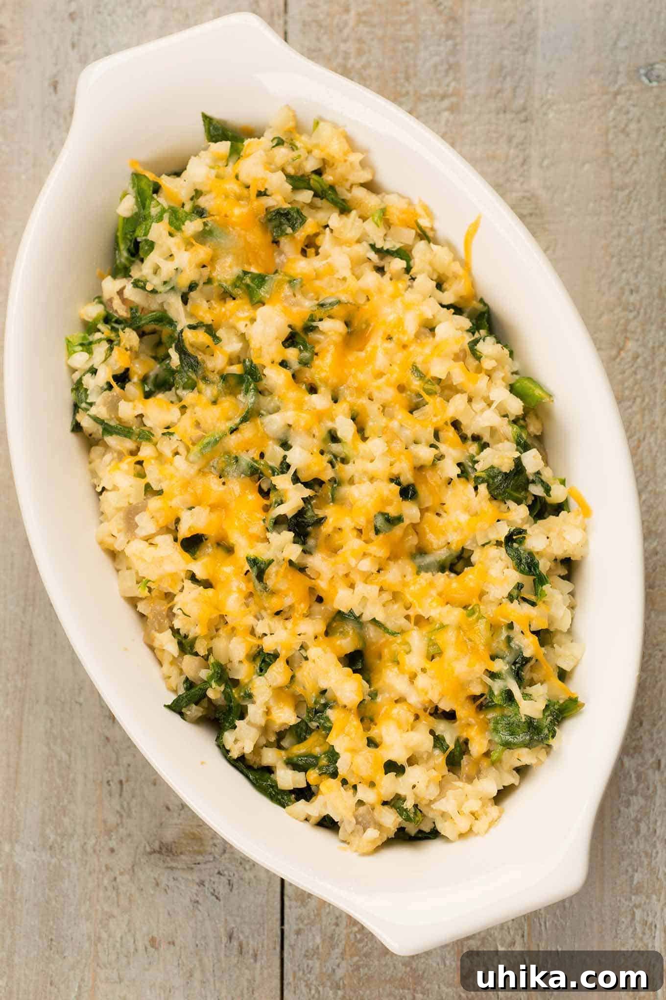 Golden Cheesy Cauliflower Gratin 3 Overhead view of a creamy riced cauliflower gratin with melted cheese and spinach in a white oval dish.