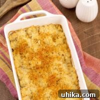 Golden Cheesy Cauliflower Gratin 4 A white, oblong casserole dish of crumb-topped, riced cauliflower gratin on a tea towel with white salt and pepper shakers in the background.