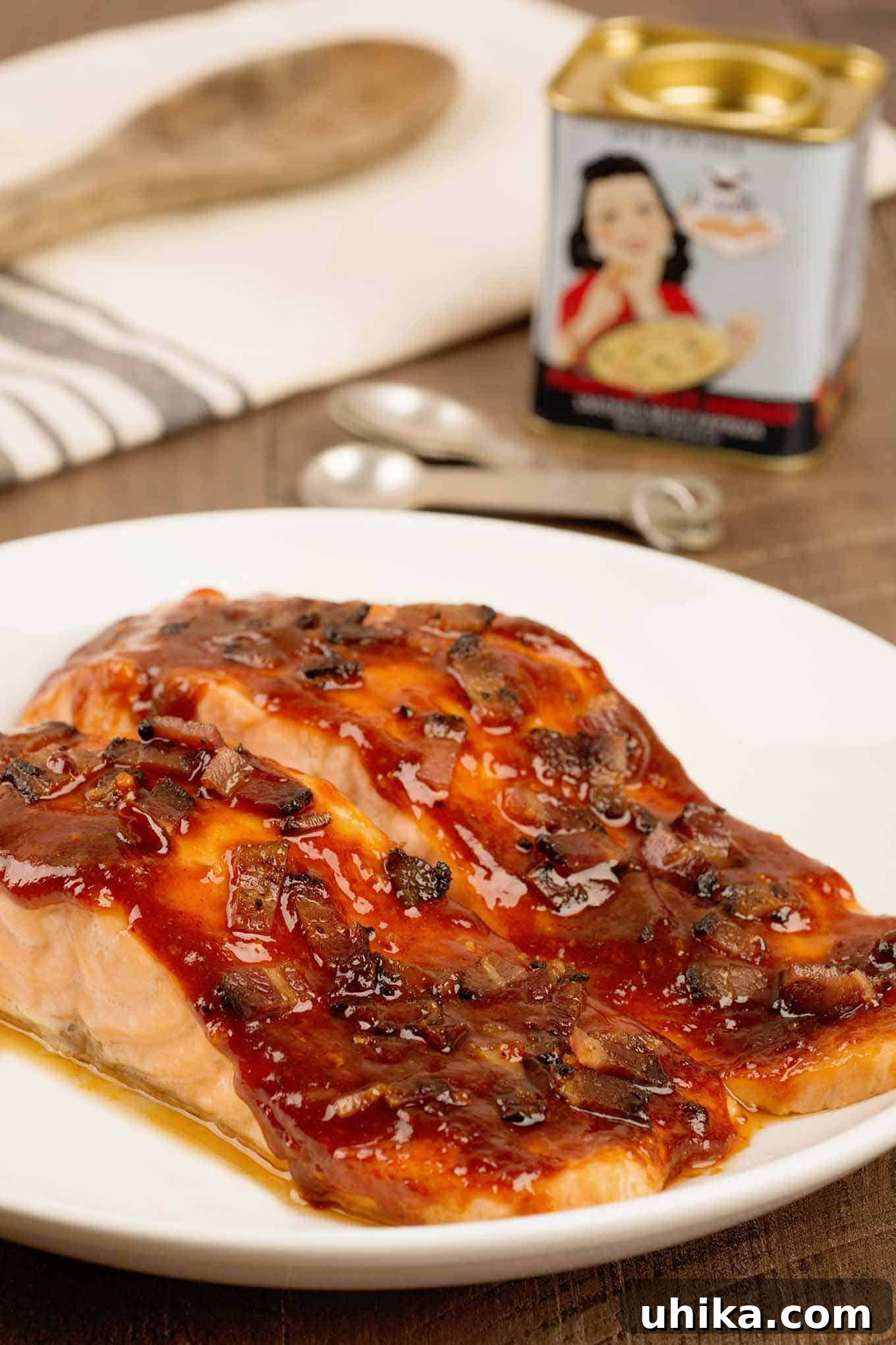 Two salmon fillets on a serving plate topped with a smoky bacon glaze, a tin of Spanish smoked paprika and measuring spoons in the background.