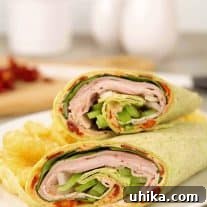 A sandwich wrap filled with sliced turkey, ham, green pepper, provolone cheese, and a sun-dried tomato spread.