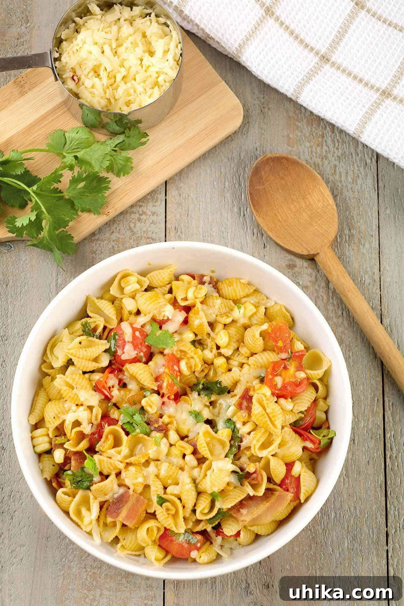 Smoky Southwest Chipotle Pasta 2 A vibrant serving bowl of Southwest Chipotle Pasta, richly adorned with crispy bacon, sweet corn, juicy tomatoes, and fresh cilantro. A cutting board with extra cilantro and a spoon sits alongside the bowl, hinting at the dish's fresh ingredients.