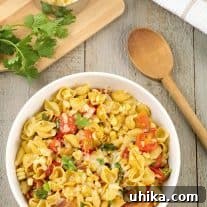 Smoky Southwest Chipotle Pasta 3 A serving bowl of pasta shells with bacon, corn, tomatoes, chipotle, cheese, and Southwest seasonings, with a cutting board, cilantro, and spoon to the side.