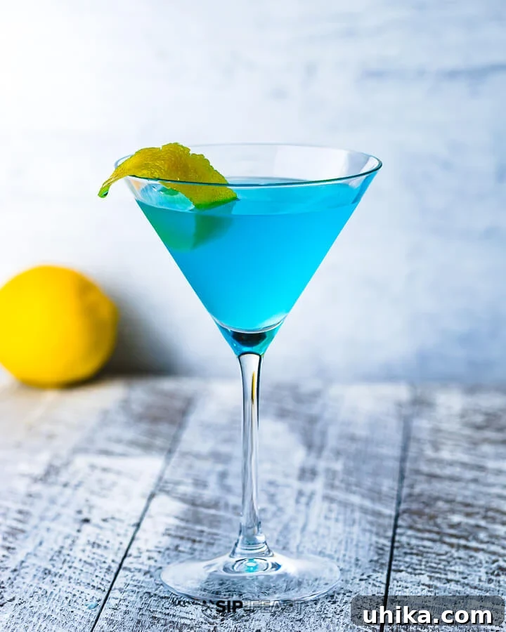 A martini glass with the Angelo Azzurro cocktail and a lemon in the background.
