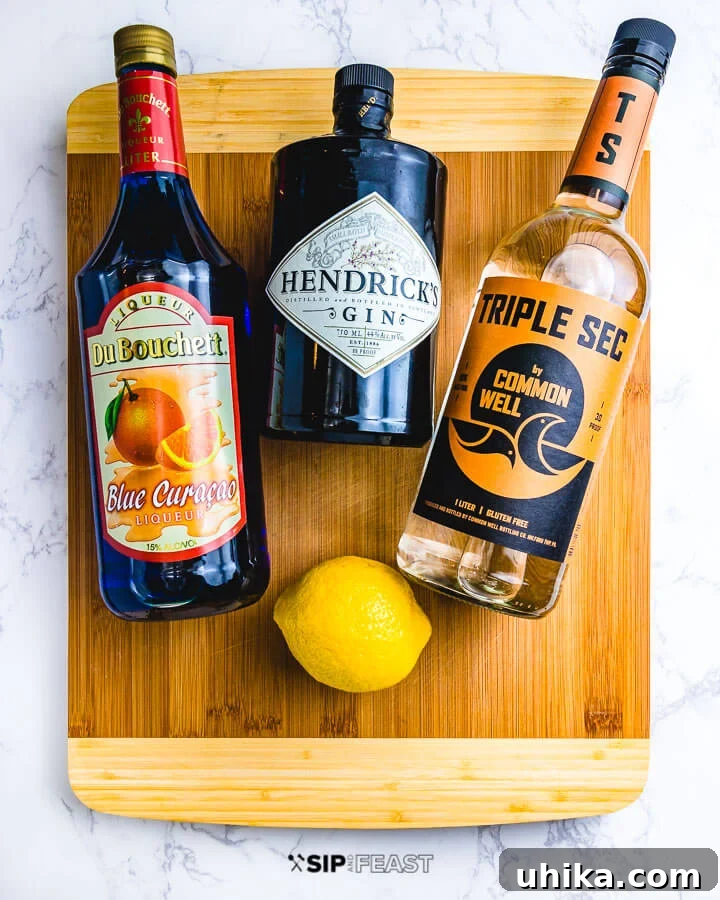 Bottles of blue curacao, gin, triple sec and a lemon on a cutting board.