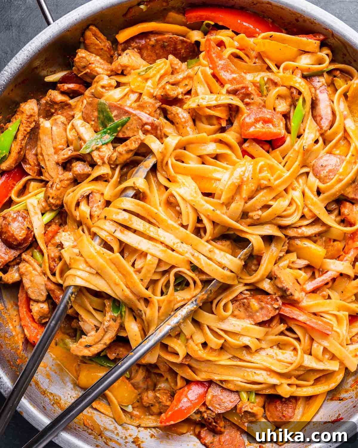 Spicy Creamy Cajun Chicken Pasta 2 Creamy Cajun chicken pasta in large pan with metal tongs, garnished with fresh herbs.