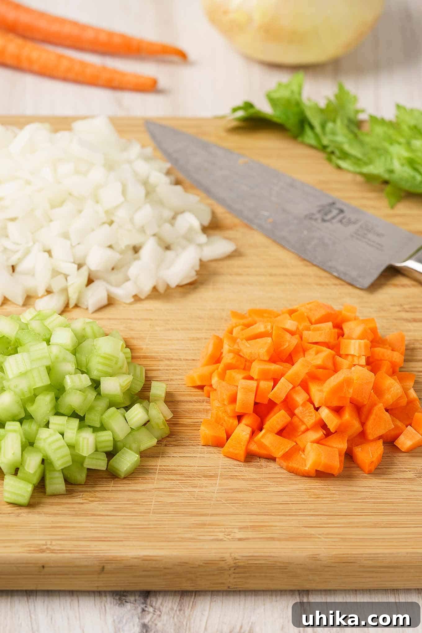 Mastering Mirepoix 2 Mirepoix ingredients (diced onion, celery, and carrots) ready on a wooden cutting board with a chef's knife, symbolizing the foundation of rich flavors in cooking.