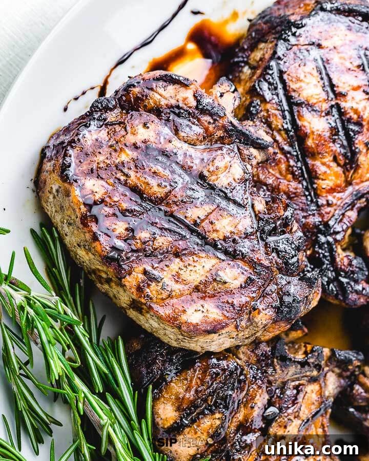 Perfectly Grilled Pork Chops 2 Perfectly grilled pork chop garnished with fresh rosemary on a white plate, ready to serve.
