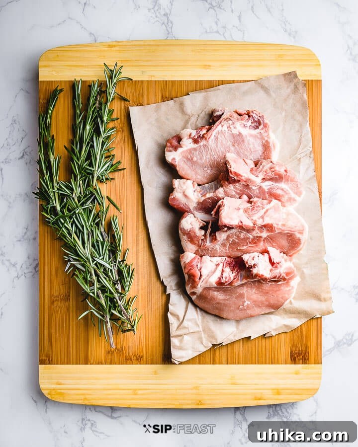 Perfectly Grilled Pork Chops 3 Four raw center-cut pork chops arranged on a wooden cutting board with a sprig of fresh rosemary.