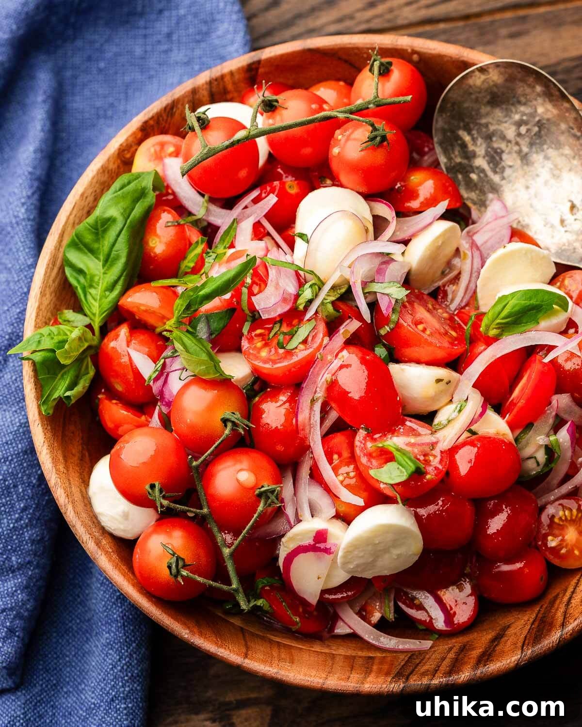 Caprese Delight 2 Fresh Tomato Mozzarella Salad in a rustic wooden bowl, garnished with basil and served with a blue linen napkin.