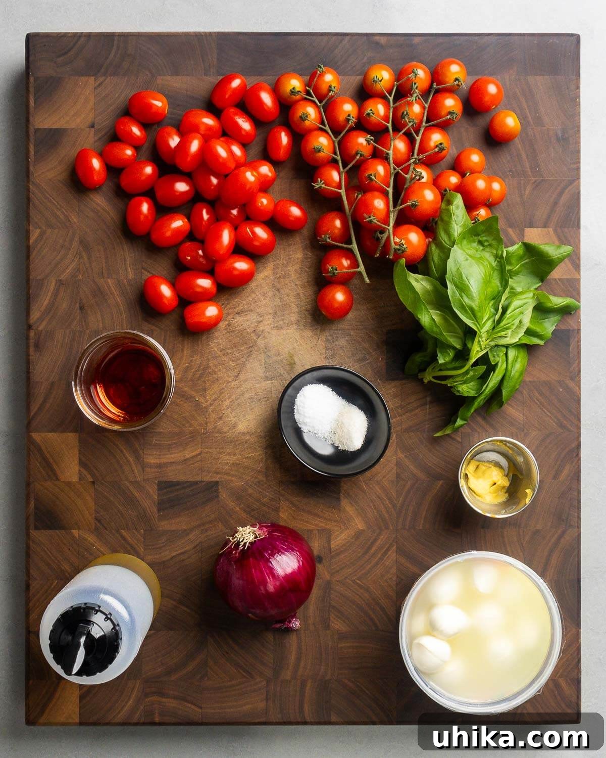 Caprese Delight 3 Ingredients for Tomato Mozzarella Salad: cherry tomatoes, fresh basil, red wine vinegar, salt, pepper, Dijon mustard, olive oil, red onion, and mozzarella balls arranged on a wooden board.