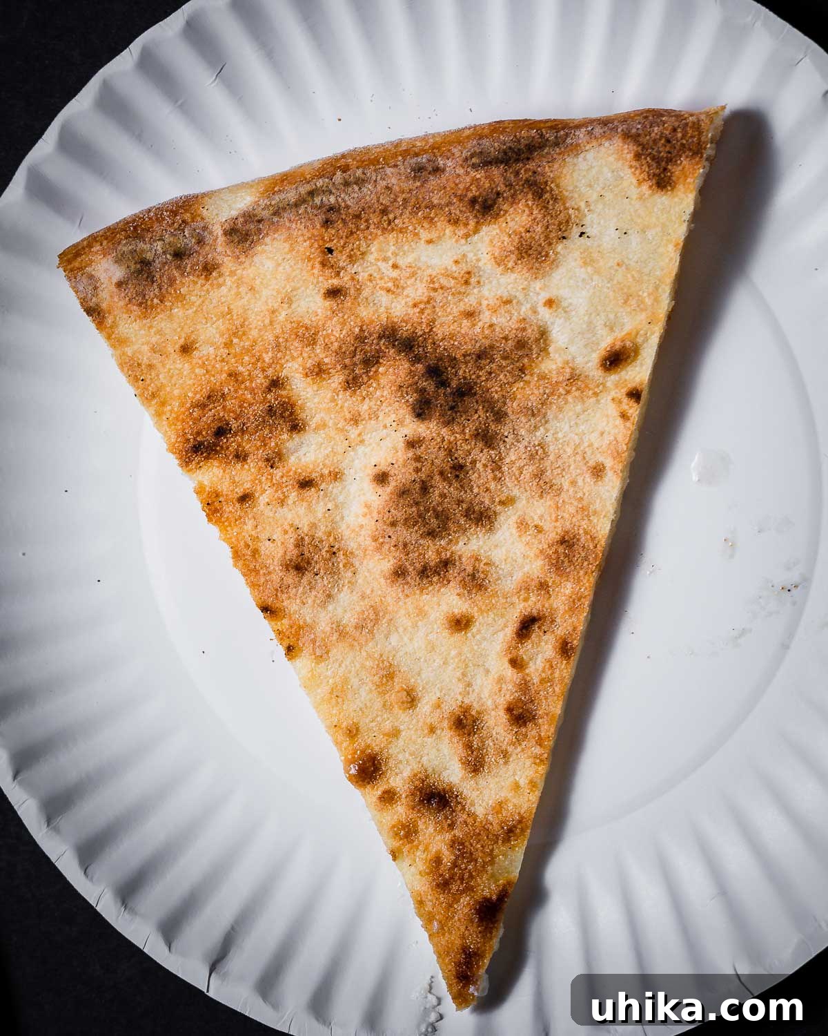 Creamy Garlic New York White Pizza 11 Close-up of the perfectly charred, leopard-spotted bottom crust of a New York white pizza slice, indicating ideal baking.