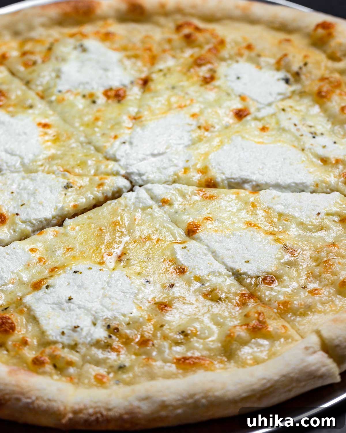 Creamy Garlic New York White Pizza 8 A full, circular New York white pizza resting in a pizza pan, its cheese perfectly melted and crust golden.