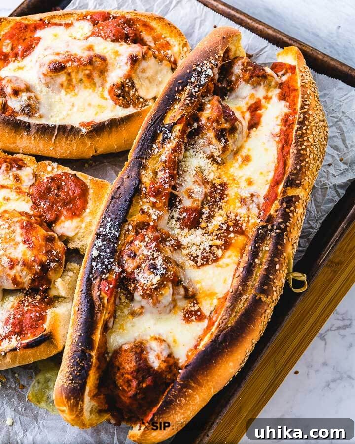 Homemade Meatball Parm Hero Recipe Three perfectly toasted meatball parm heroes lined up on a baking sheet, bubbling with melted cheese and rich sauce, ready to serve.