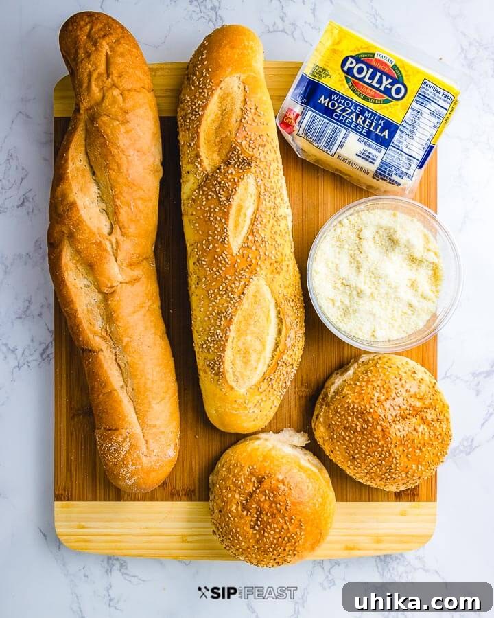 Meatball Parm Hero Ingredients Essential ingredients for a meatball parm hero: two loaves of crusty Italian bread, a fresh block of mozzarella cheese, and a small bowl of grated Parmesan.