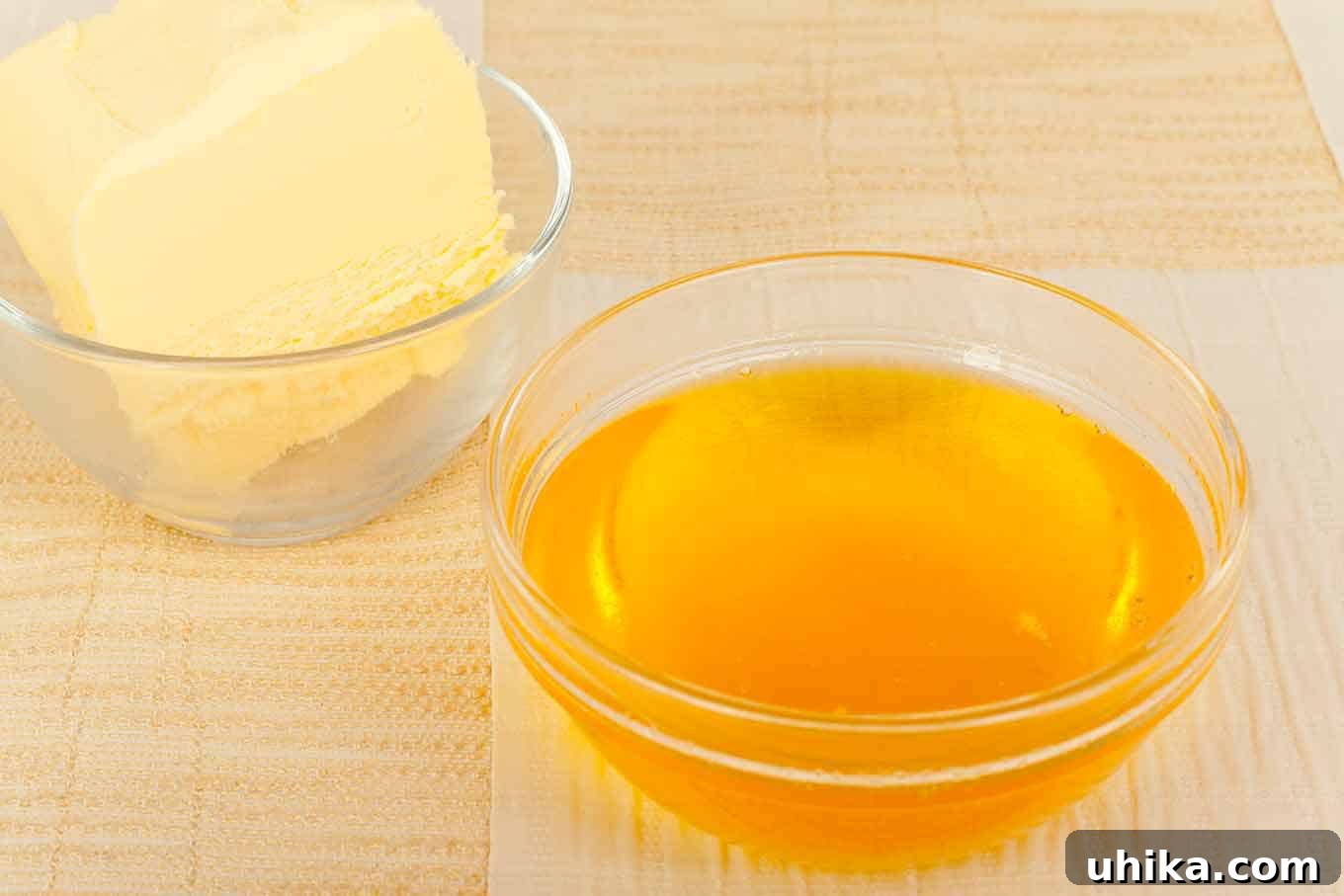 Mastering Clarified Butter 2 A small, clear glass dish of golden clarified butter with a second dish of solid regular butter in the background, illustrating the transformation.