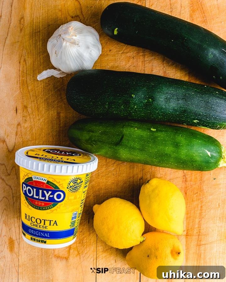 Creamy Ricotta Stuffed Zucchini 3 Fresh ingredients laid out on a wooden cutting board, showcasing the main components: vibrant green zucchini, bright yellow lemons, a container of creamy ricotta cheese, and cloves of fresh garlic.