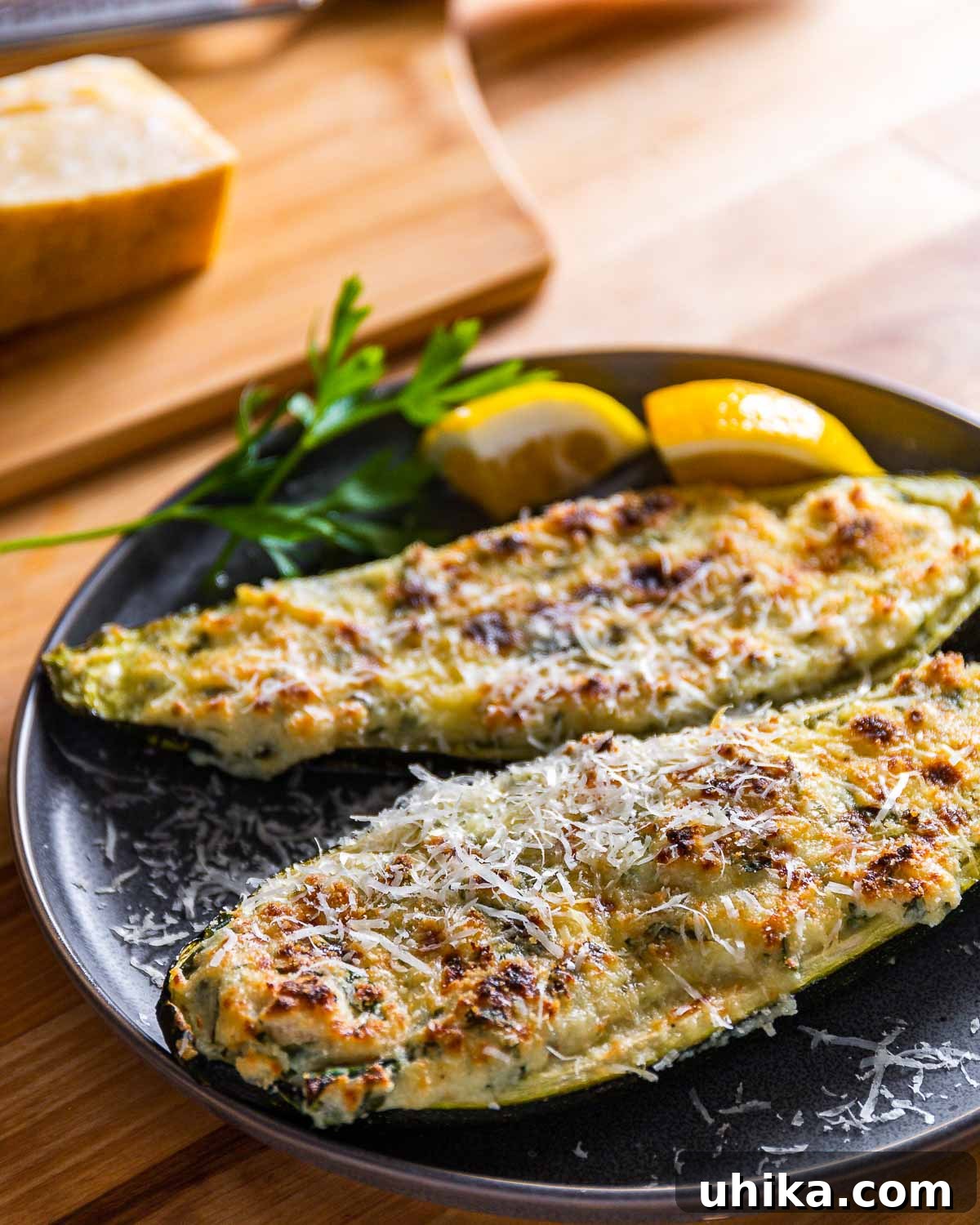 Creamy Ricotta Stuffed Zucchini 6 Two beautifully broiled Lemon Ricotta Stuffed Zucchini Boat halves, garnished with fresh lemon wedges and vibrant parsley, served elegantly on a grey plate.