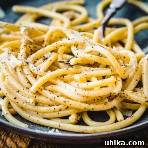 Peppery Cheese Bucatini 3 Bucatini cacio e pepe on a plate with a fork, ready to be eaten.