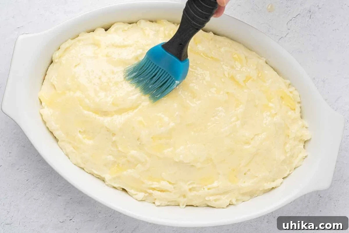 Hearty Lamb Shepherd's Pie 6 White oval casserole with fully assembled shepherd's pie being brushed with melted butter before baking.