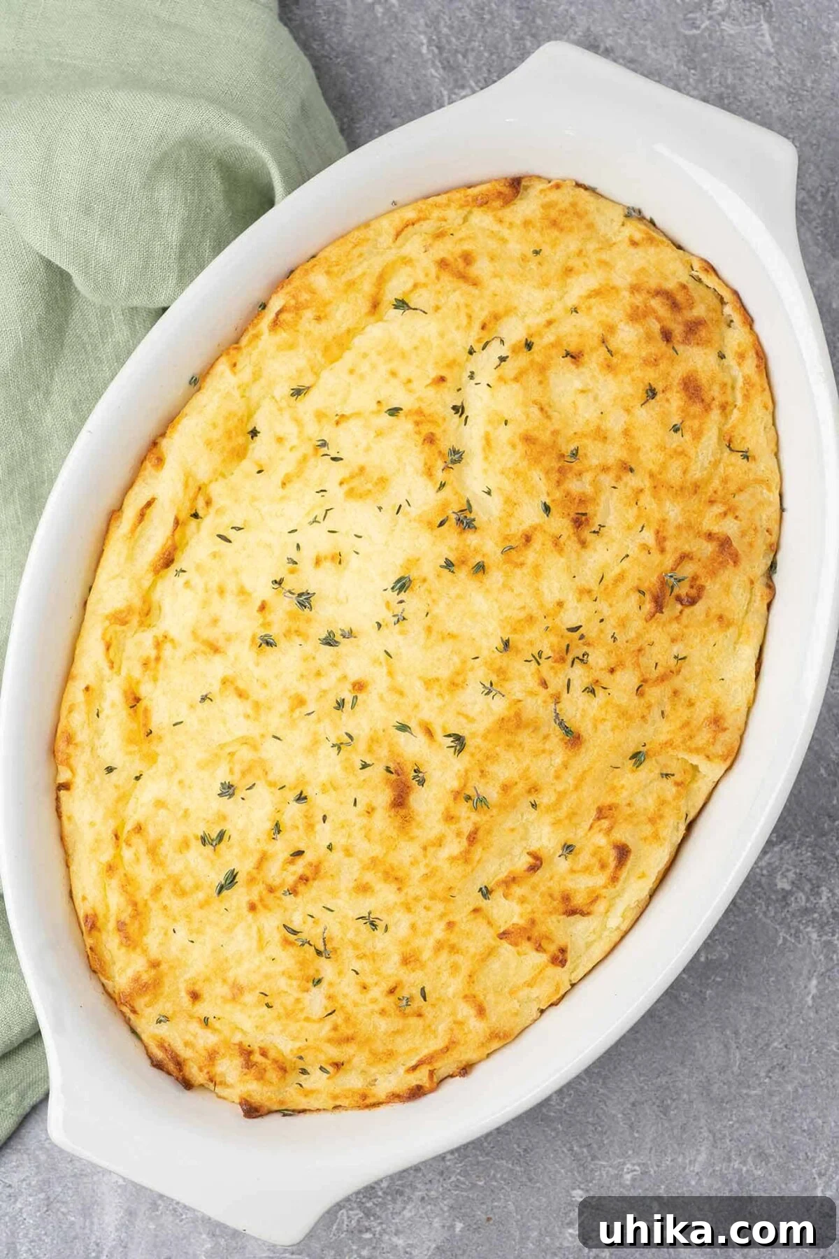 Hearty Lamb Shepherd's Pie 7 Fully baked, uncut shepherd's pie in a white oval casserole with fresh thyme sprinkled on top for garnish.