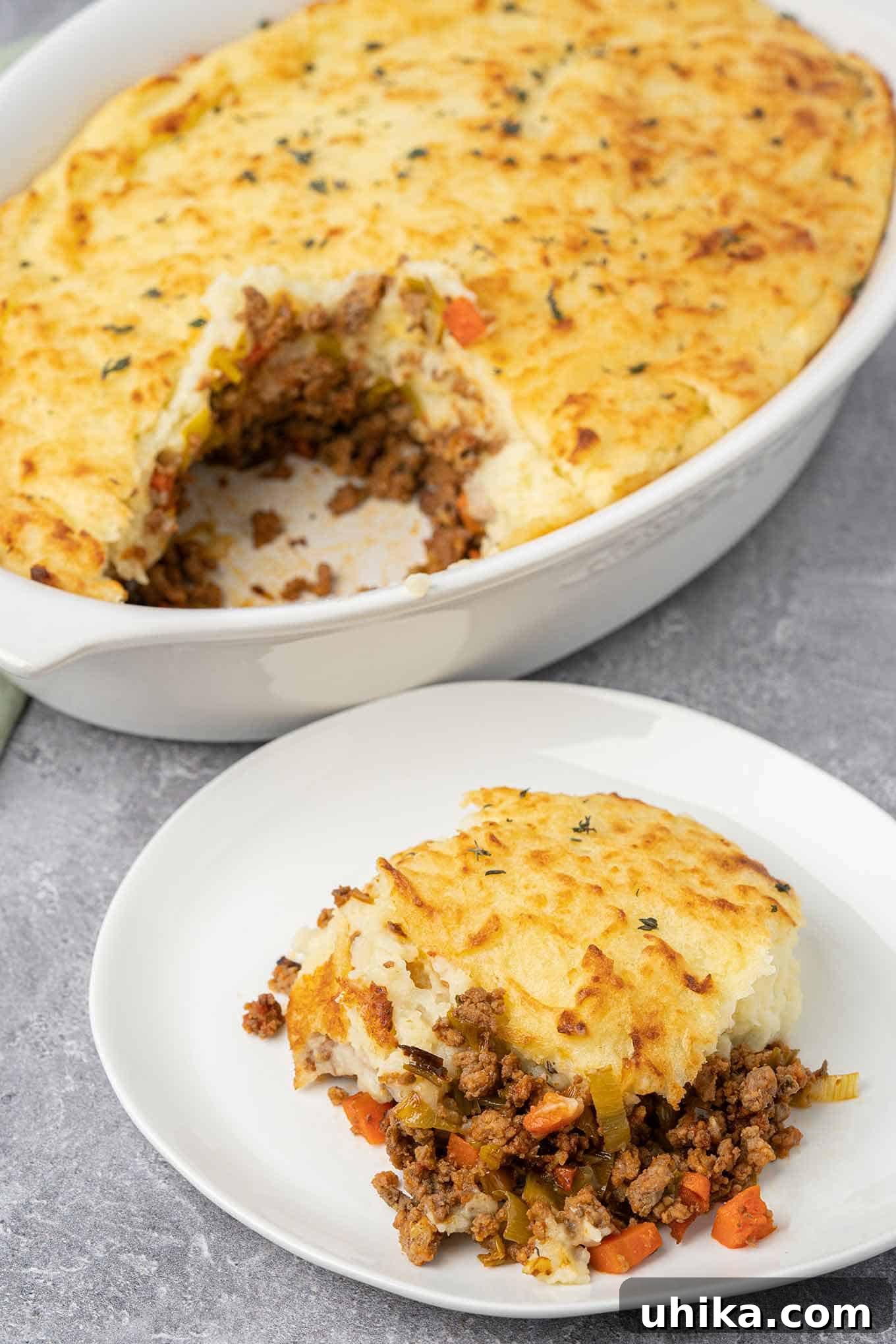 Hearty Lamb Shepherd's Pie 8 A serving of shepherd's pie on a plate with the partially cut casserole in the background.
