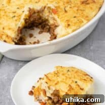 A serving of Shepherd's Pie on a plate with the casserole in the background.