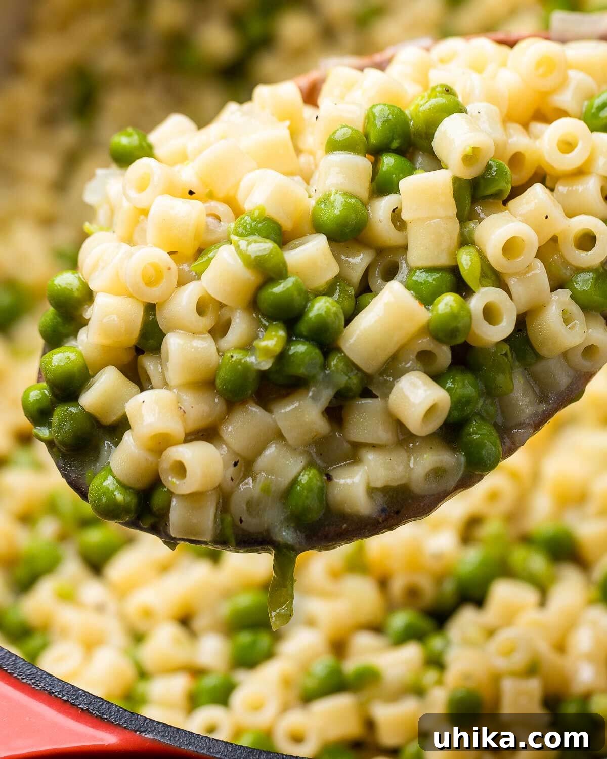 Sweet Pea Pasta 7 A large wooden ladle elegantly holds a generous serving of creamy Pasta e Piselli over a rustic Dutch oven, highlighting the dish's rich texture and inviting warmth.