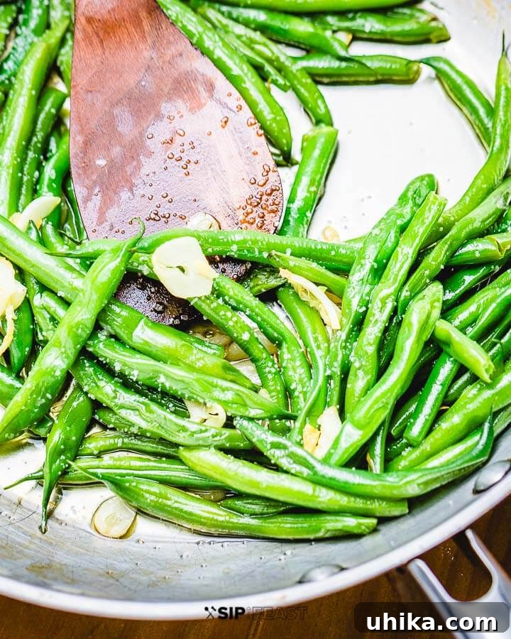 Italian Green Beans - sipandfeast.com #italian #greenbeans #sidedish Sauteed garlic string beans in pan with wooden spoon. Freshly cooked Italian green beans with garlic and olive oil in a skillet.