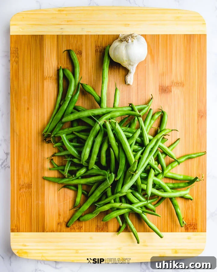 Italian Green Beans - sipandfeast.com #italian #greenbeans #sidedish Fresh green beans and garlic head on cutting board. Ingredients laid out before preparation for Italian green beans.
