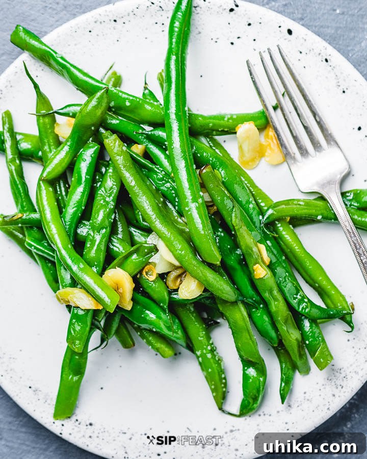 Italian Green Beans - sipandfeast.com #italian #greenbeans #sidedish Garlic green beans on white plate. A serving of Italian green beans with garlic and oil on a white plate, ready to be enjoyed.