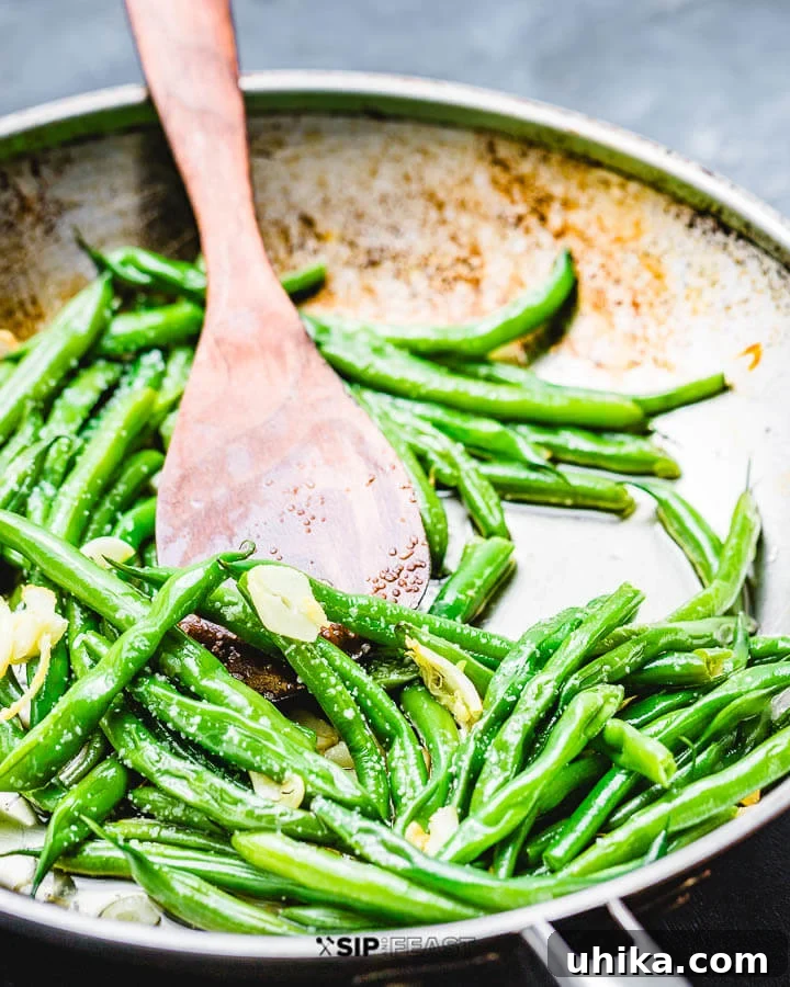 Italian Green Beans - sipandfeast.com #italian #greenbeans #sidedish String beans with garlic and oil in pan on blue background. Close-up of cooked Italian green beans in a pan, infused with garlic and olive oil.