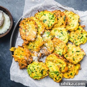 Crispy Italian Zucchini Fritters 2 Italian zucchini fritters on parchment paper lined plate.