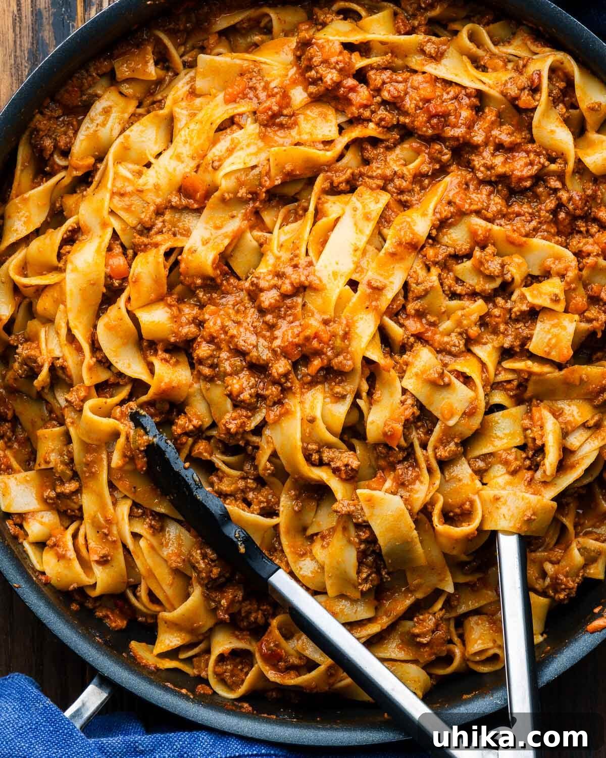 Pappardelle Bolognese An Elevated Classic 2 A generous serving of Pappardelle Bolognese, freshly cooked and nestled in a large pan, ready to be served with tongs, highlighting the rich, hearty sauce clinging to every strand of wide pasta.